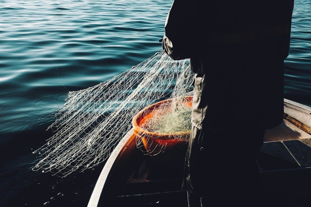 Fischer mit ausgebreitetem Netz in einem kleinen Boot auf dem See